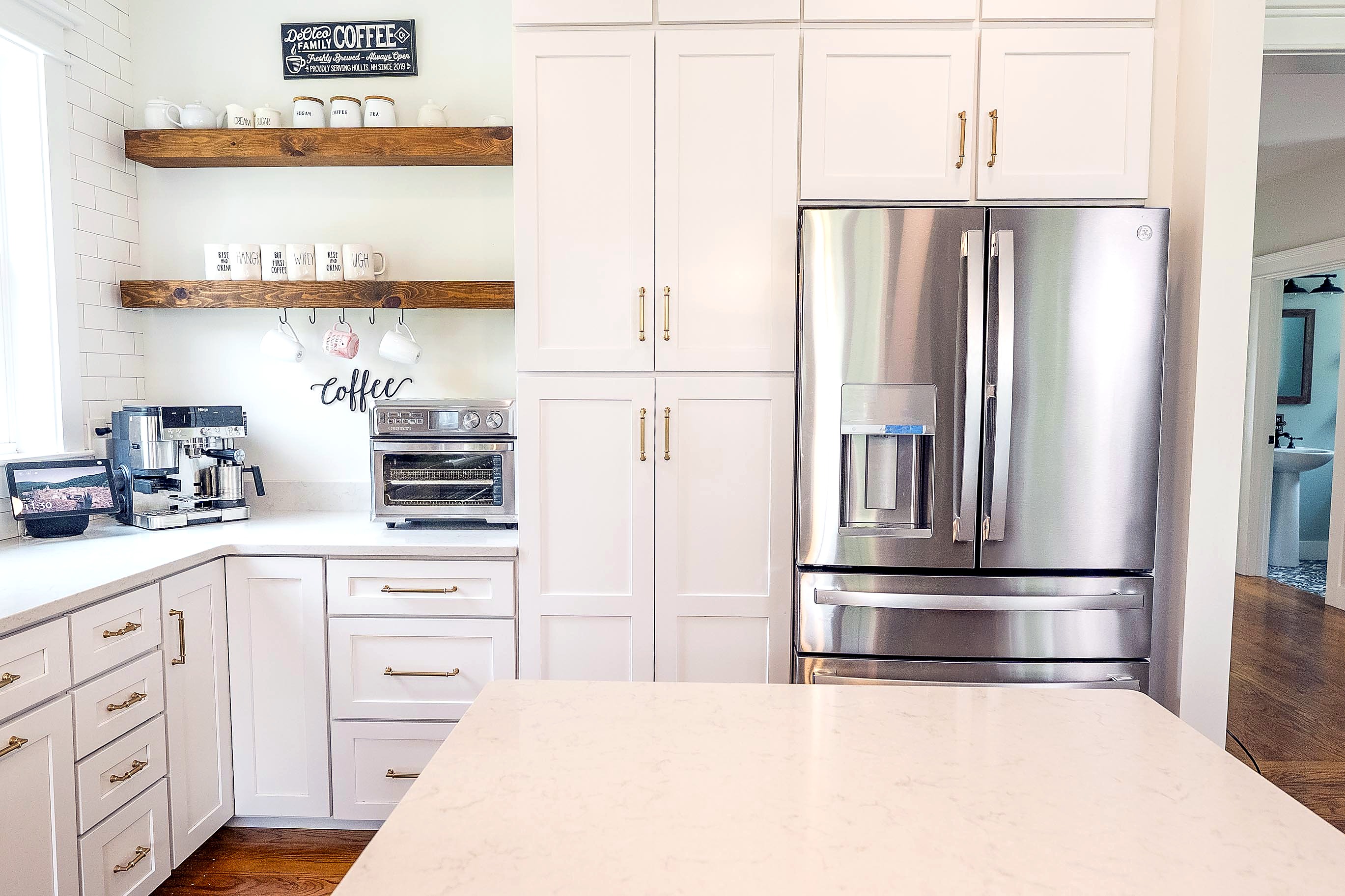Refrigerator wall with tall white cabinets and wood shelves